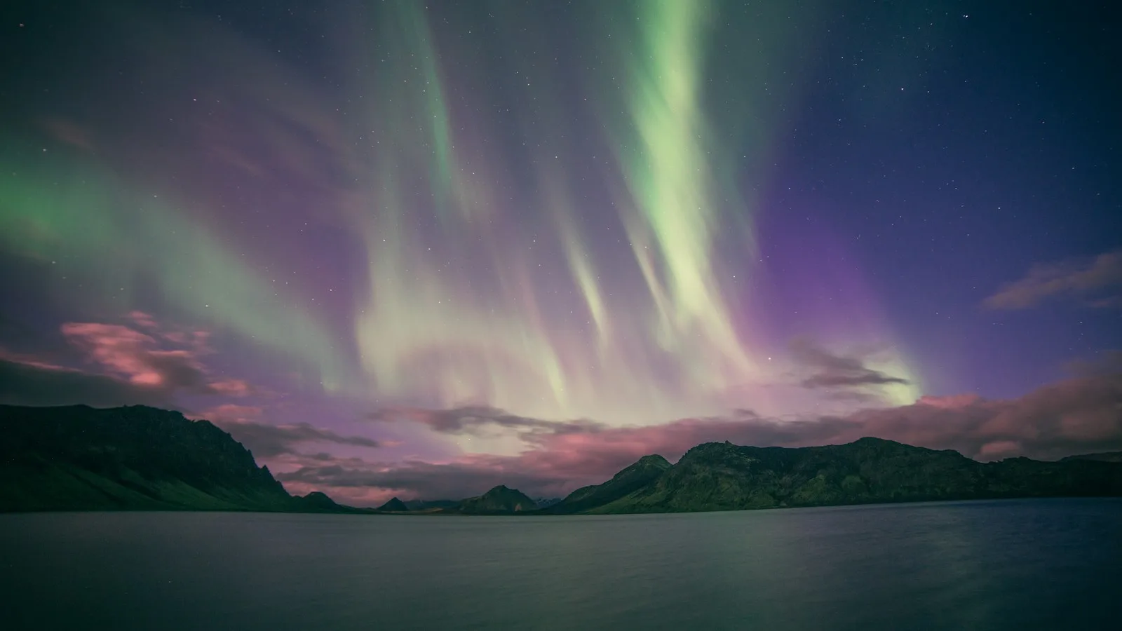 Aurores boréales vertes et violettes au-dessus d'un lac et de montagnes en Islande